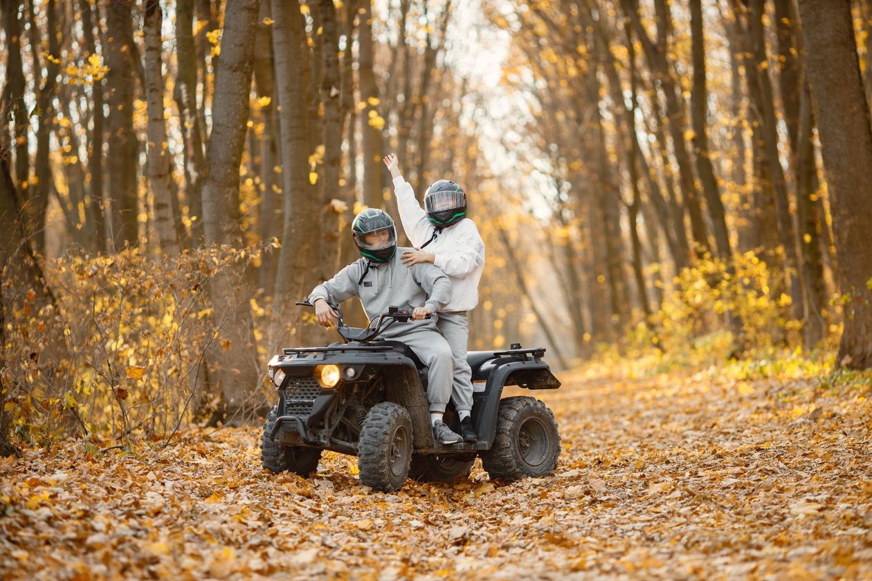 A man and a woman are riding an atv in the woods.