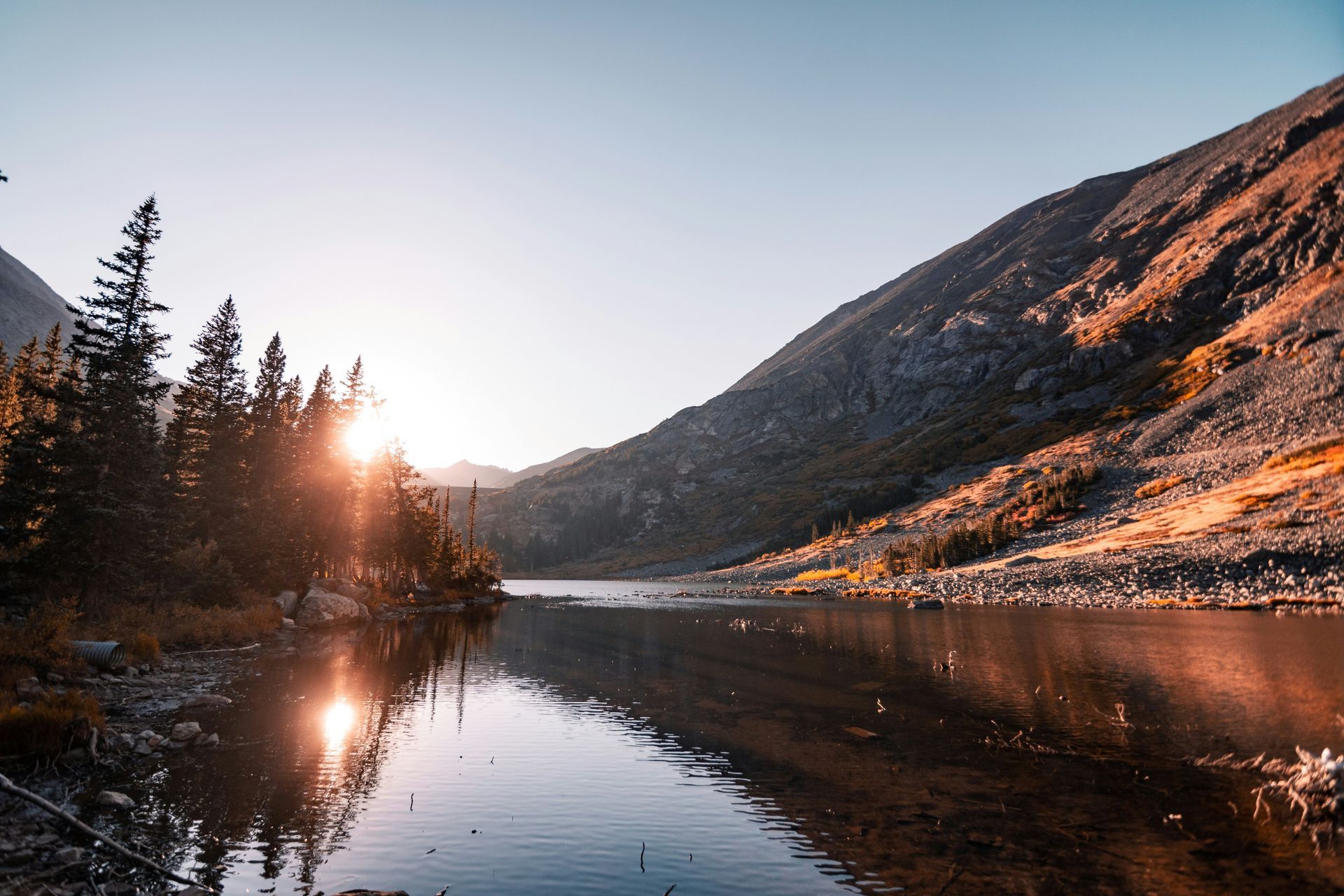 The sun is reflected in the water of a lake surrounded by mountains.