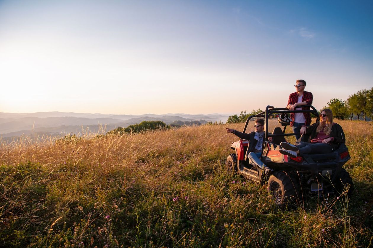 A group of people are sitting in a atv on top of a grassy hill.