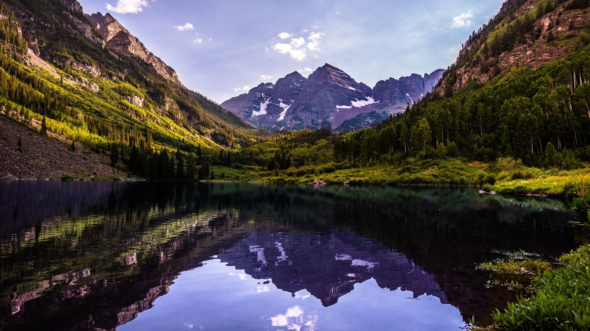 A lake in the middle of a mountain valley with mountains reflected in the water.