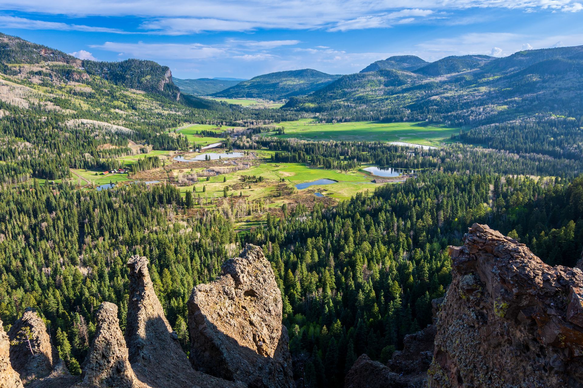 A view of a valley surrounded by mountains and trees from the top of a mountain.