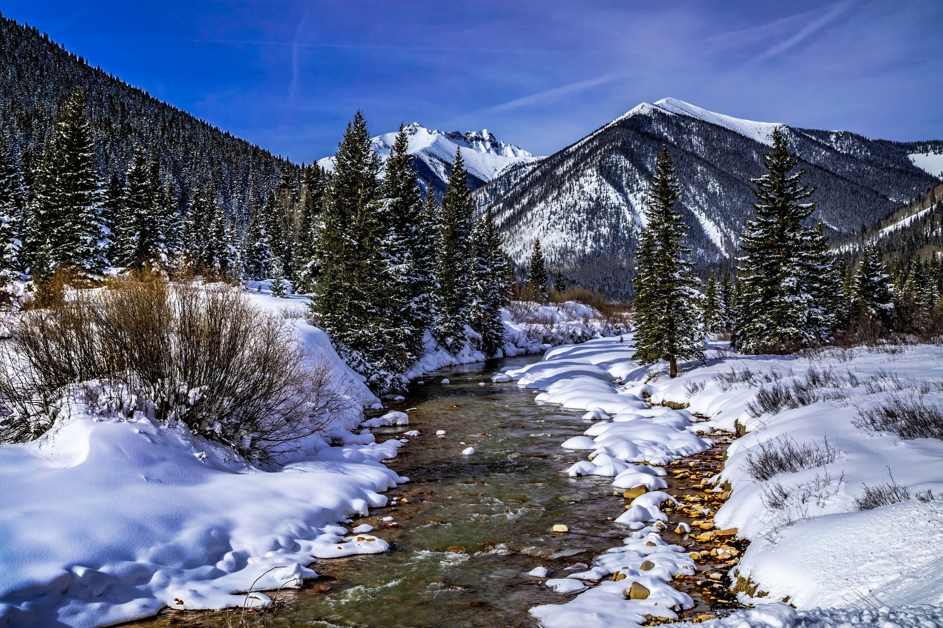 A river running through a snowy forest with mountains in the background.