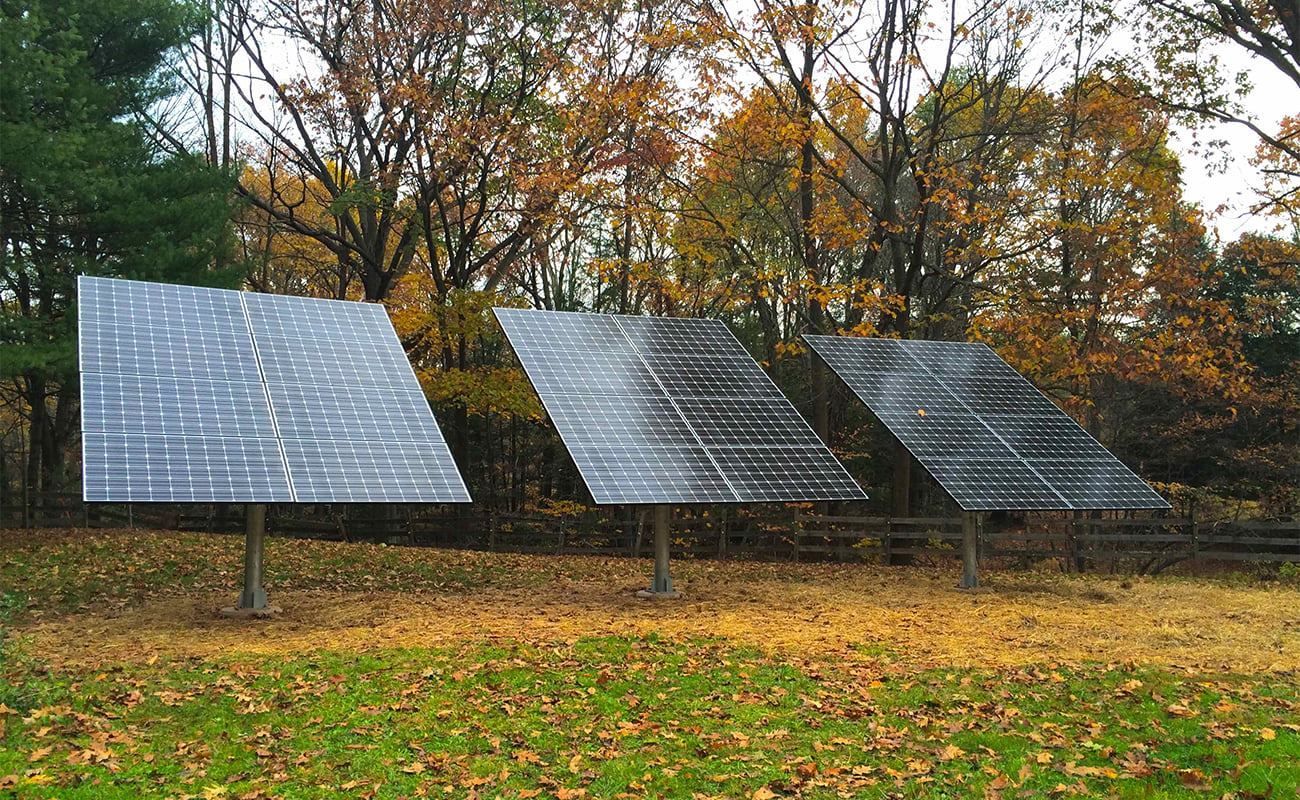Three solar panels are sitting in a field with trees in the background.