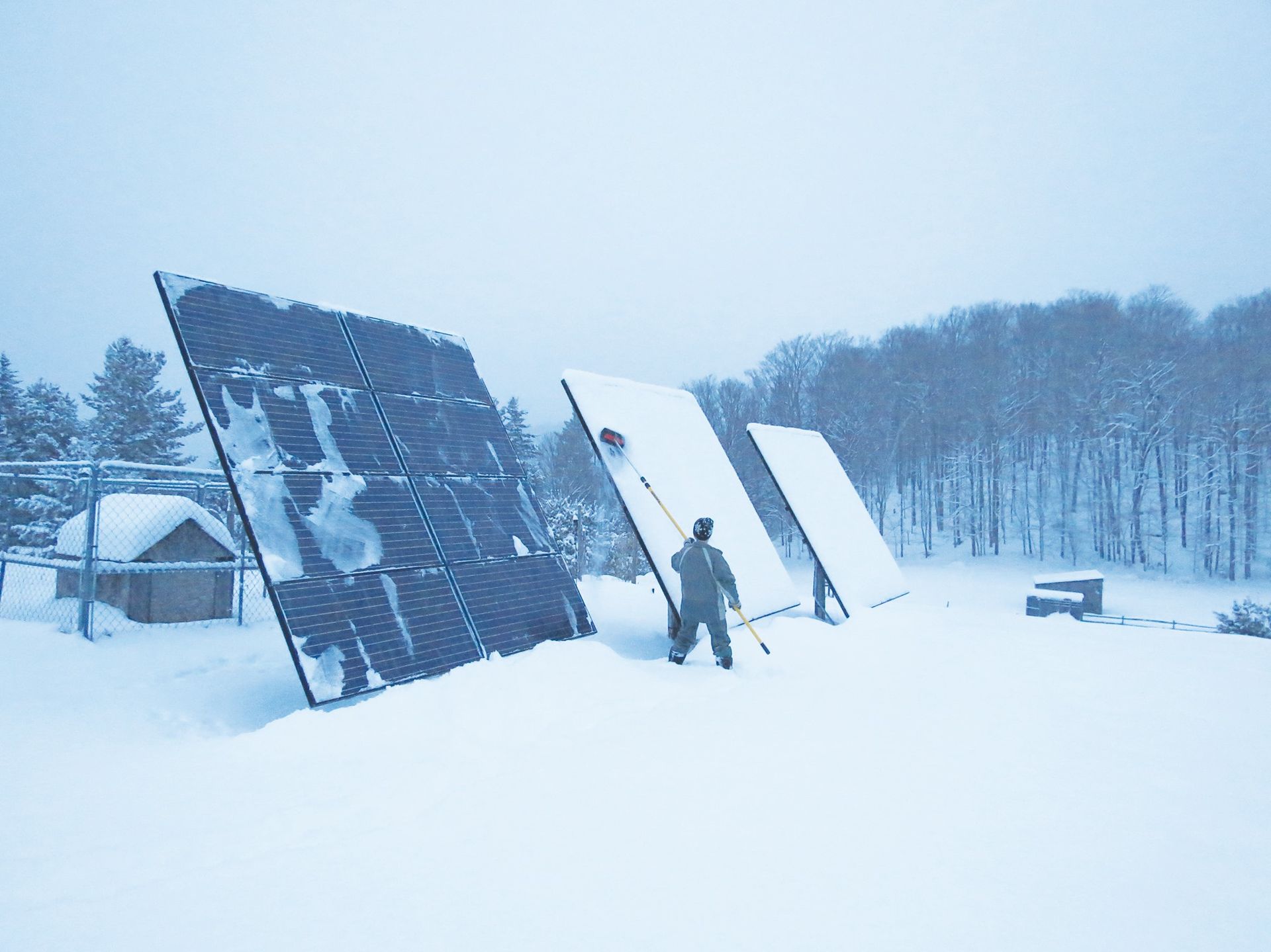 A man is standing in the snow near a row of solar panels