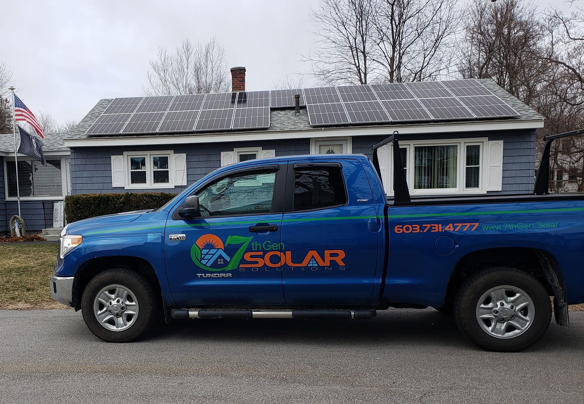 A blue solar truck is parked in front of a house with solar panels on the roof.