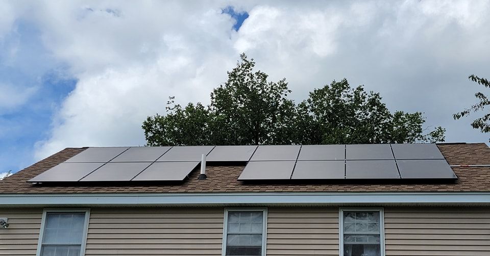 A house with solar panels on the roof and a tree in the background.