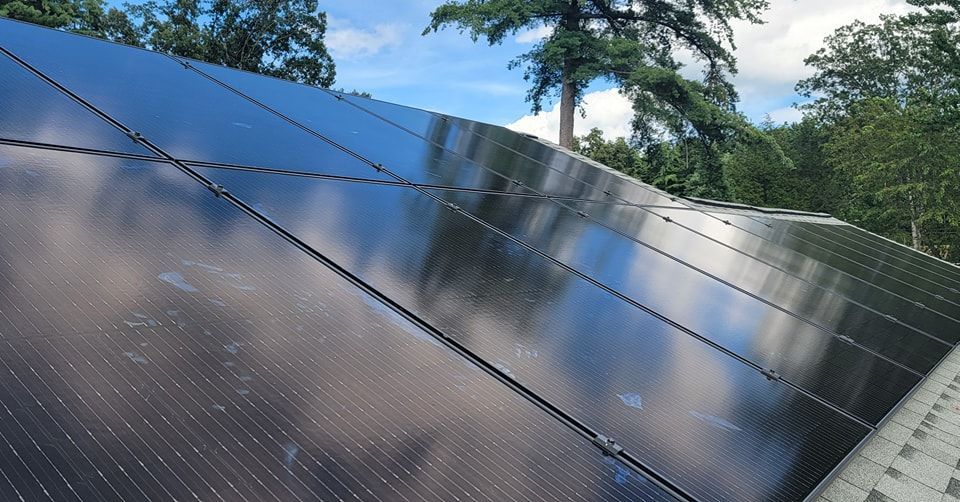 A row of solar panels on a roof with trees in the background.