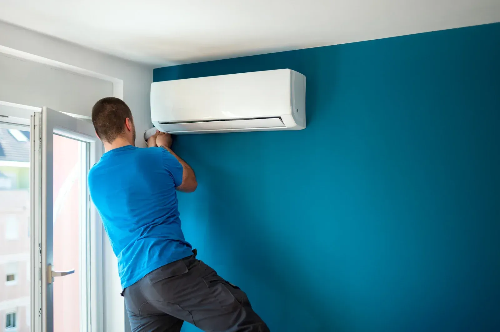 A man is installing an air conditioner on a blue wall.