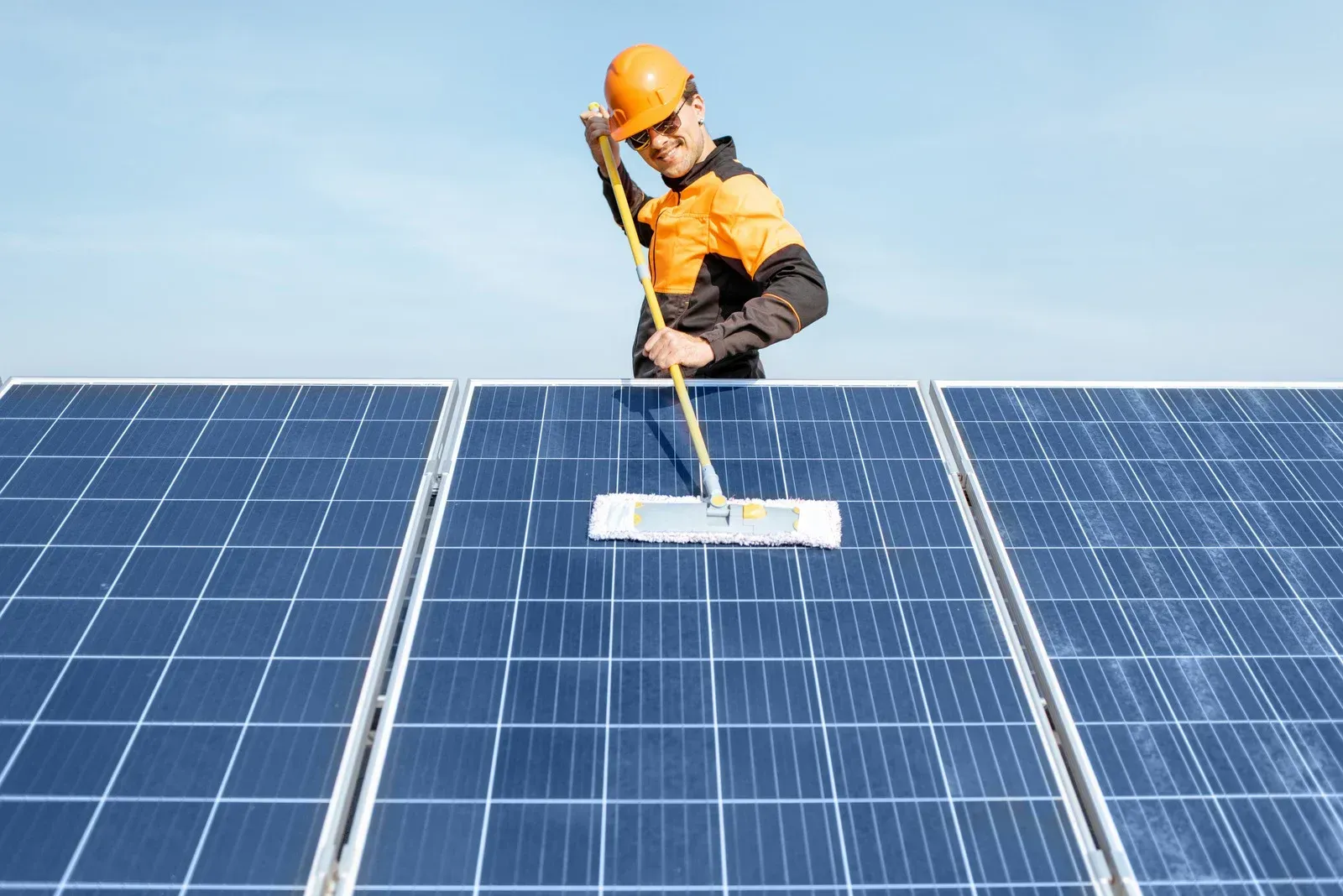 A man is cleaning solar panels with a mop.
