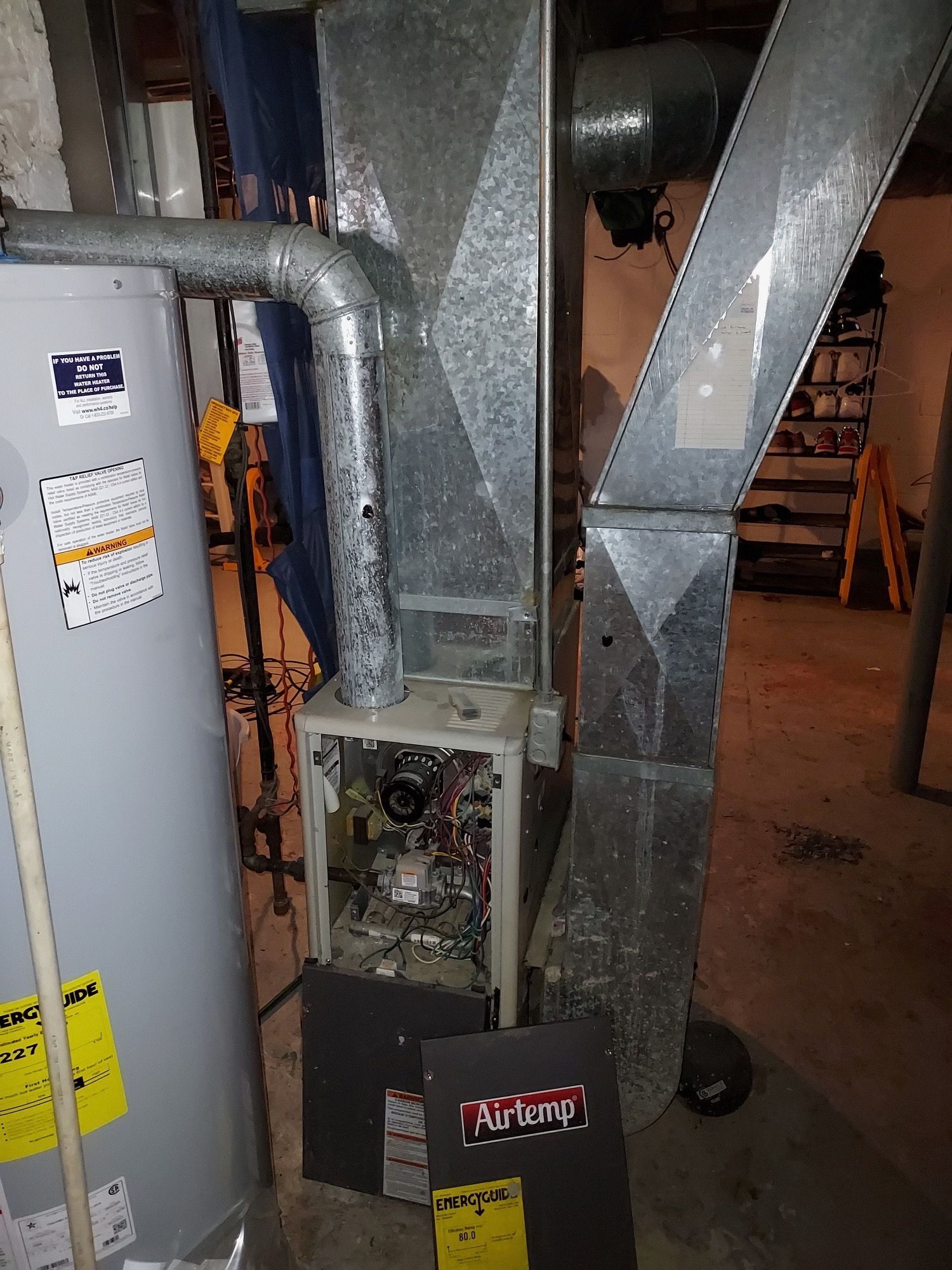 Furnace with open panels next to a water heater and ductwork in a basement setting.
