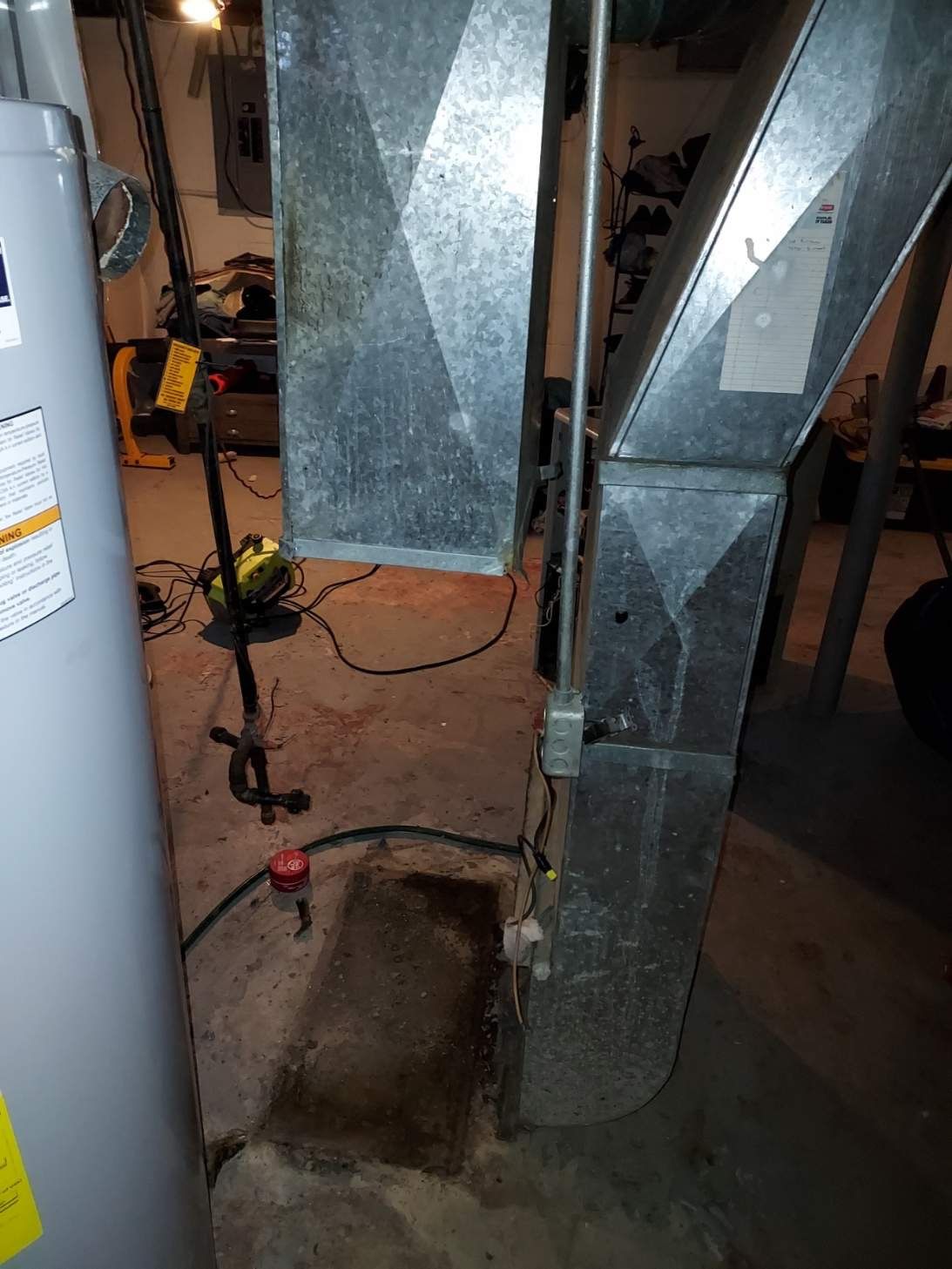 Basement with water heater, ductwork, sump pump, and standing water on concrete floor.