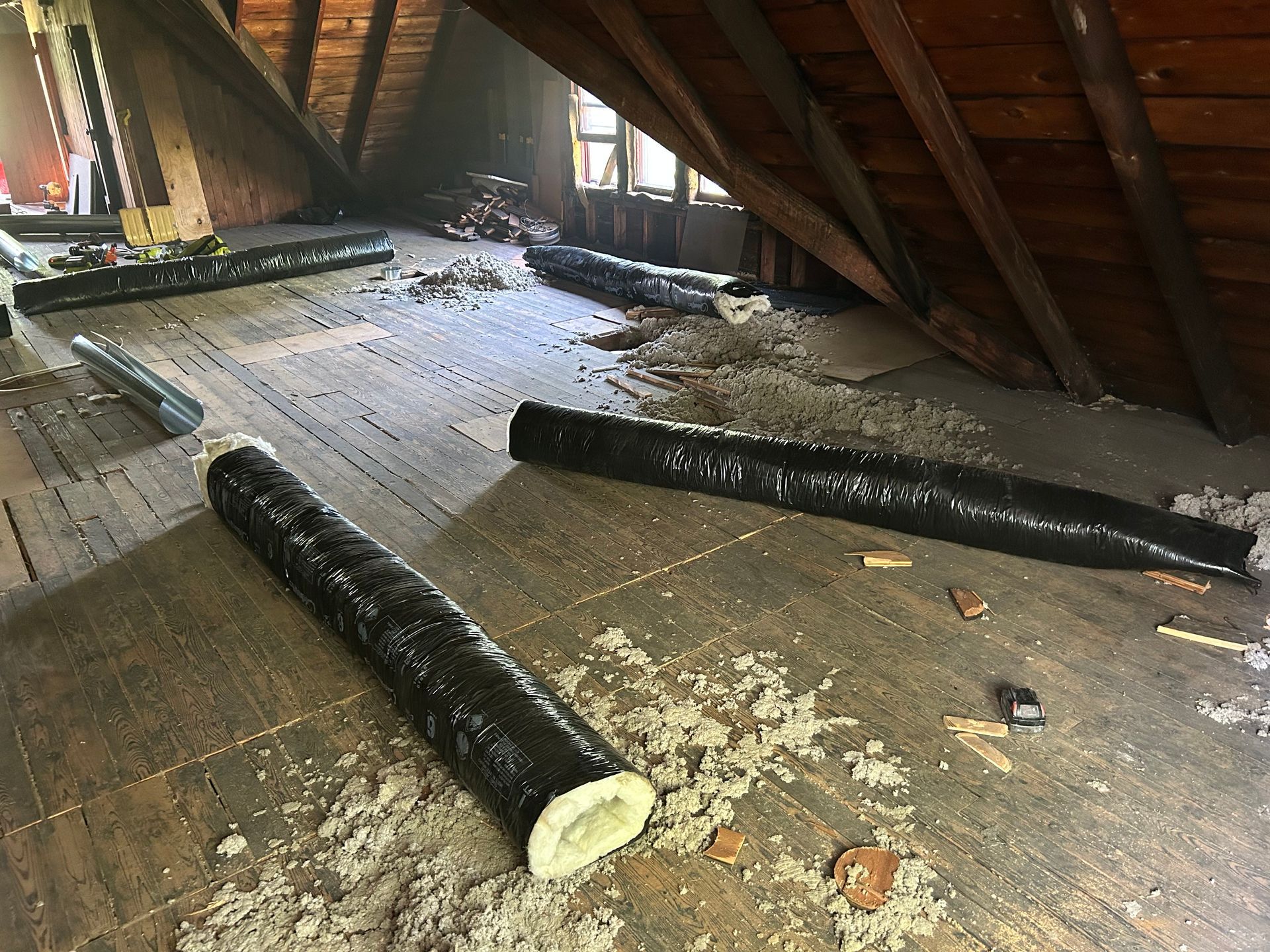 Attic with black flexible ducting, insulation, and wooden structure.