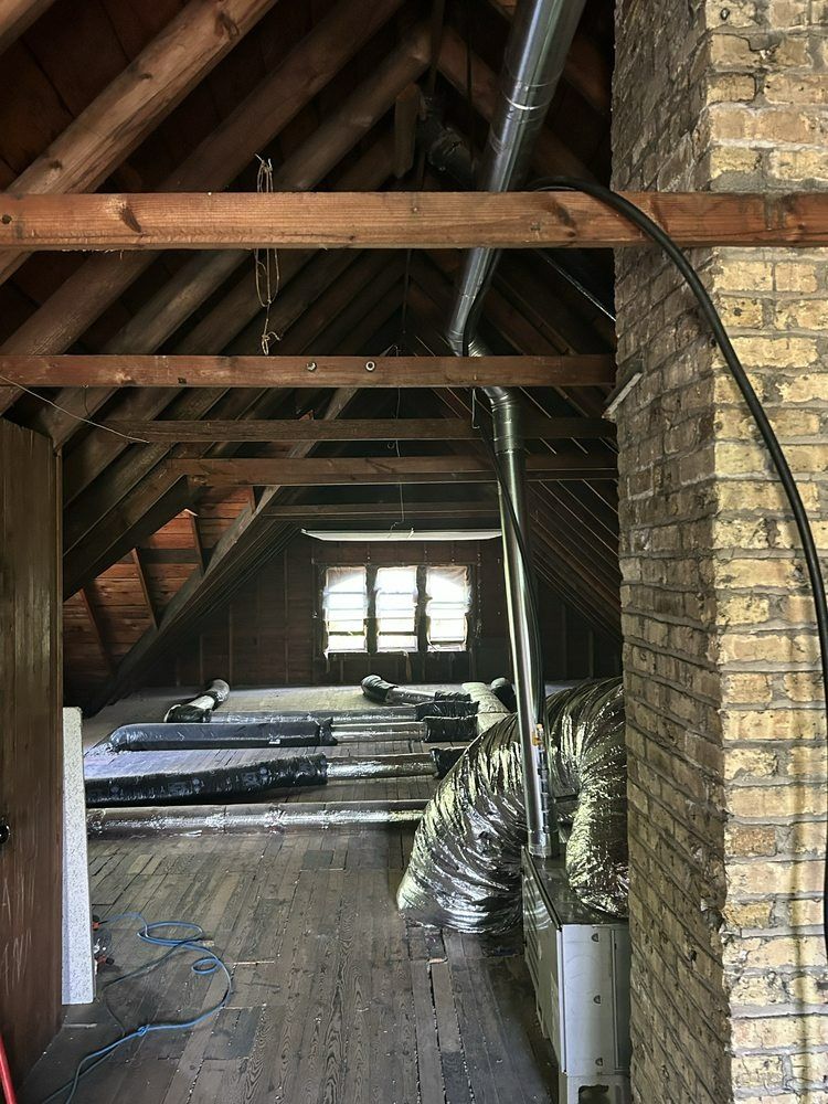 Attic with wooden beams, brick chimney, ductwork, window, and flooring in various states of completion.