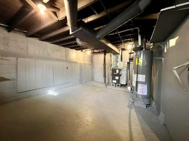 Basement with concrete floor, furnace, water heater, pipes, and wooden paneling on walls.