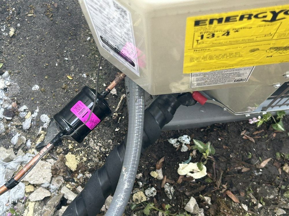 Air conditioner unit with a black component taped in place. Yellow energy efficiency label on the side.
