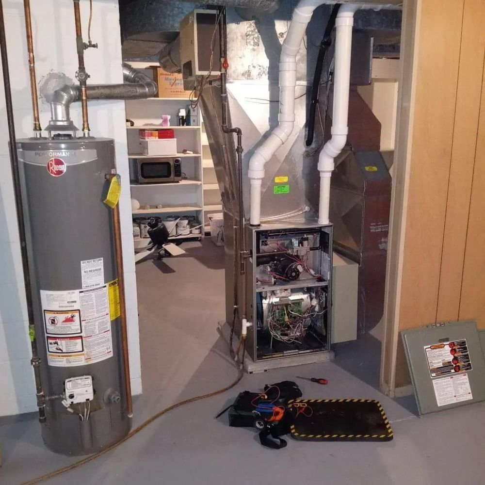 Water heater and furnace in a basement mechanical room with tools on the floor.