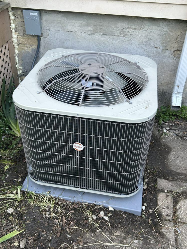 Central air conditioning unit outside a building with a fan on top.