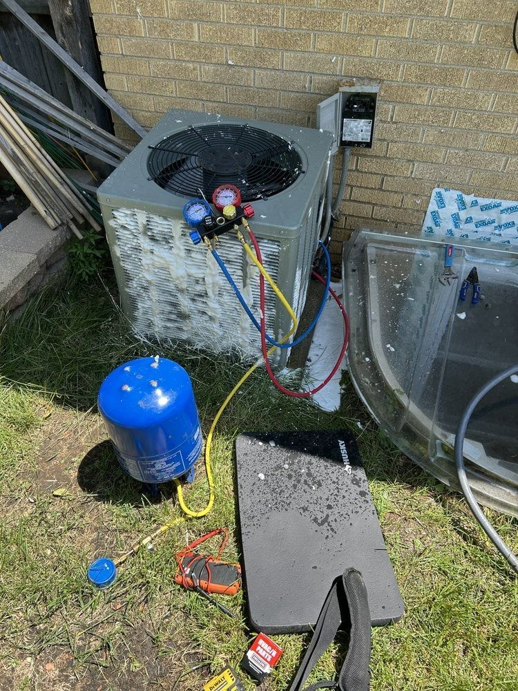 HVAC unit with gauges, connected to a blue tank on grass near a brick wall and debris.