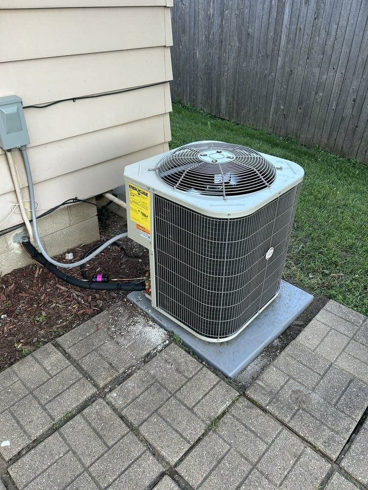 Air conditioning unit next to a house on a concrete pad; green grass and a wooden fence are visible.