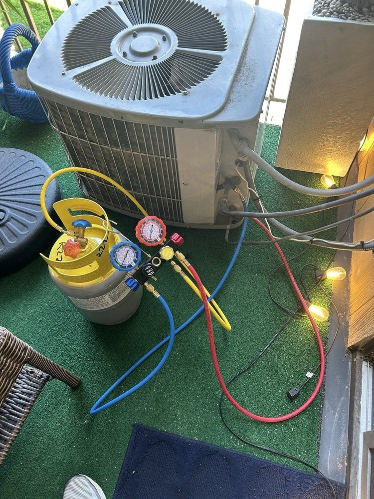 An HVAC unit with gauges connected to a yellow refrigerant tank on a green surface.
