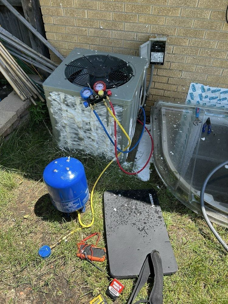 HVAC unit with gauges, connected to a blue tank and tools, next to a brick wall.