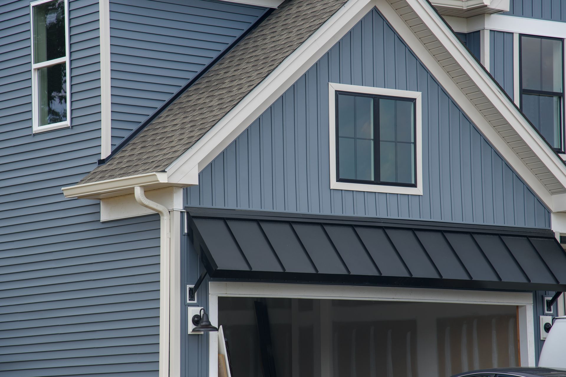 A blue house with a black roof has a car parked in the garage.