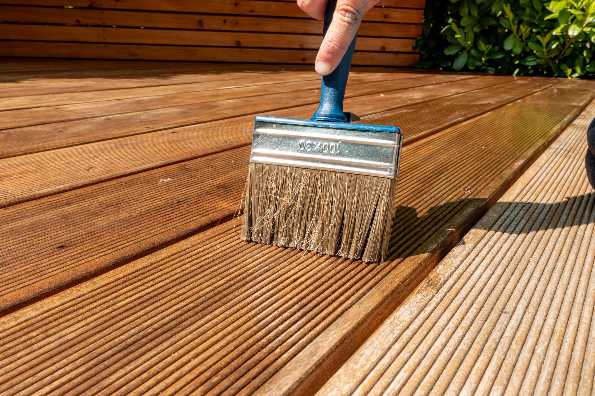 A person is painting a wooden deck with a brush.