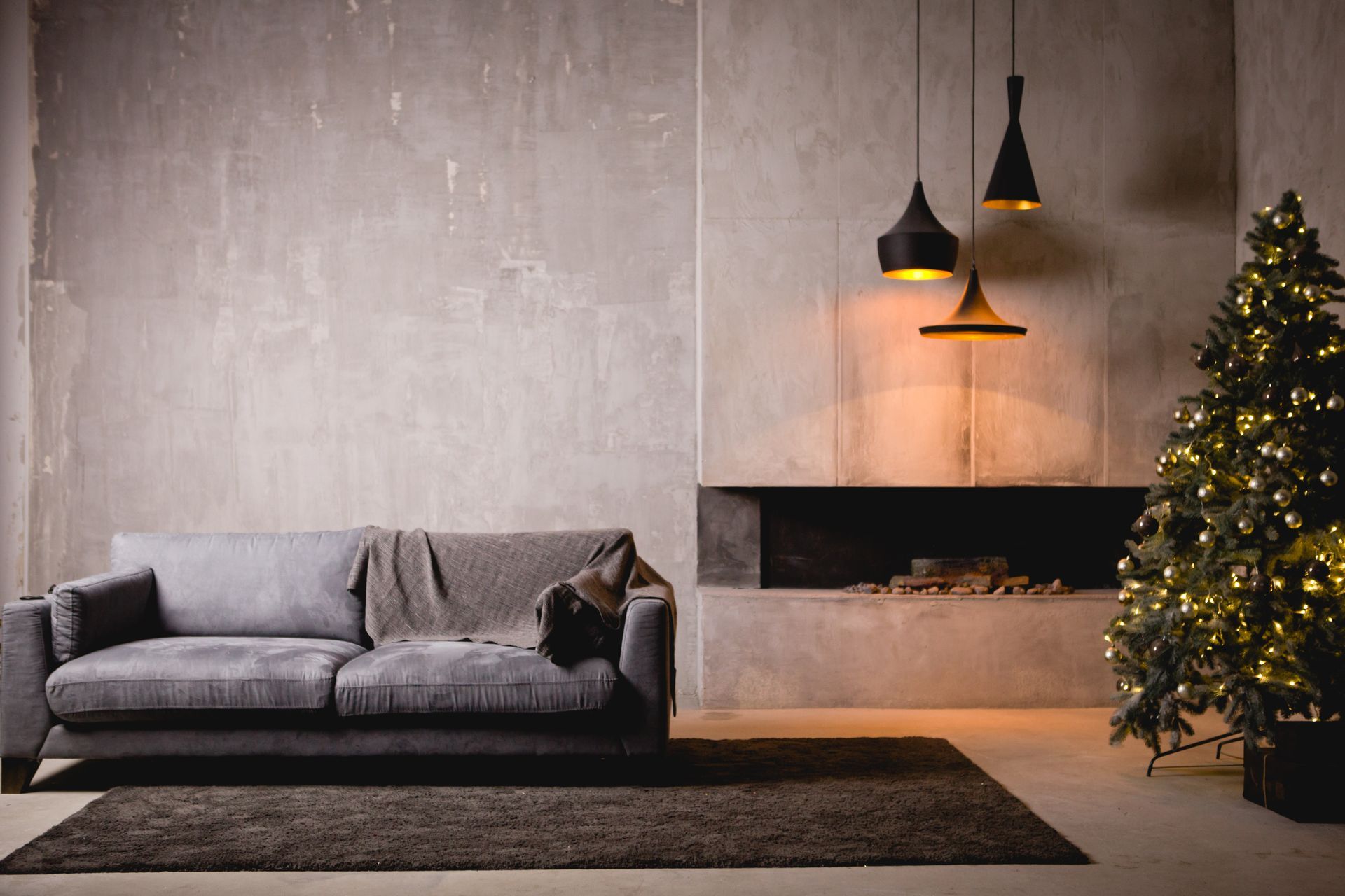 Gray sofa in minimalist living room with Christmas tree, fireplace, and hanging lights.