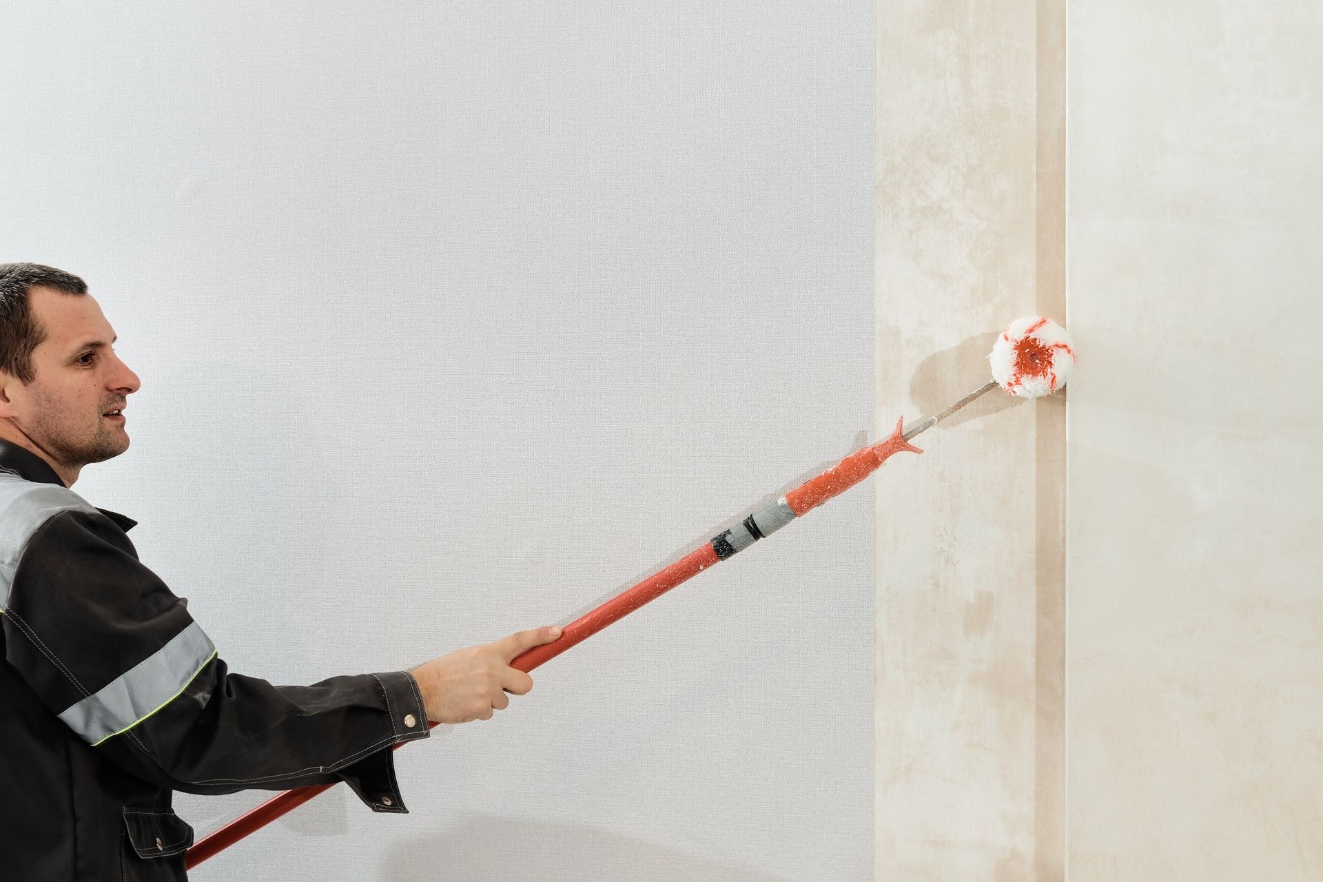 A man is painting a wall with a paint roller.