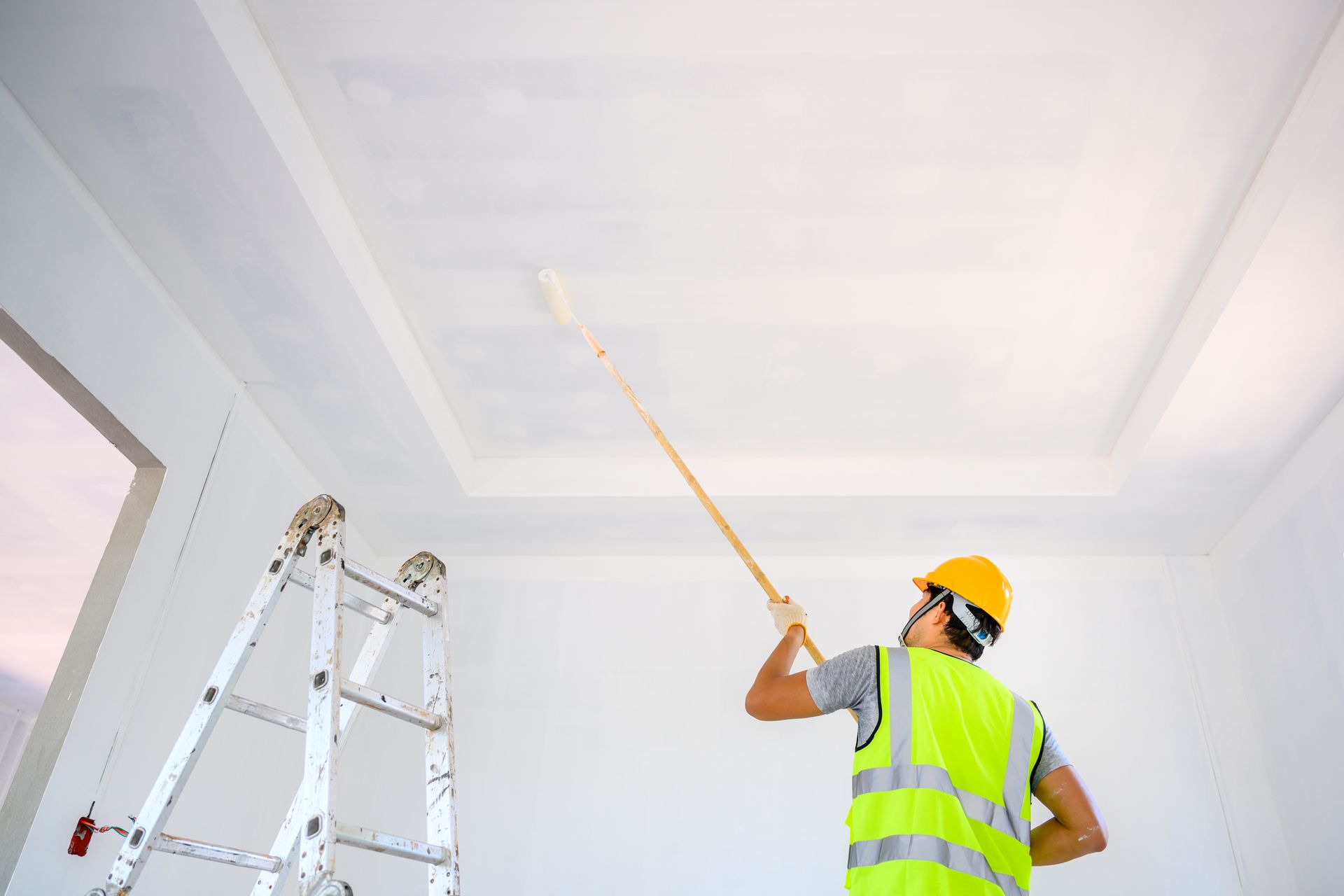 A man is painting the ceiling of a room with a roller.