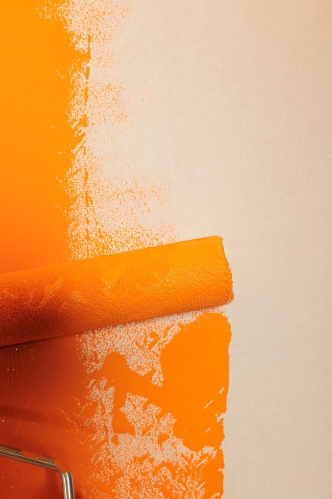 A paint roller is being used to paint a wall orange.