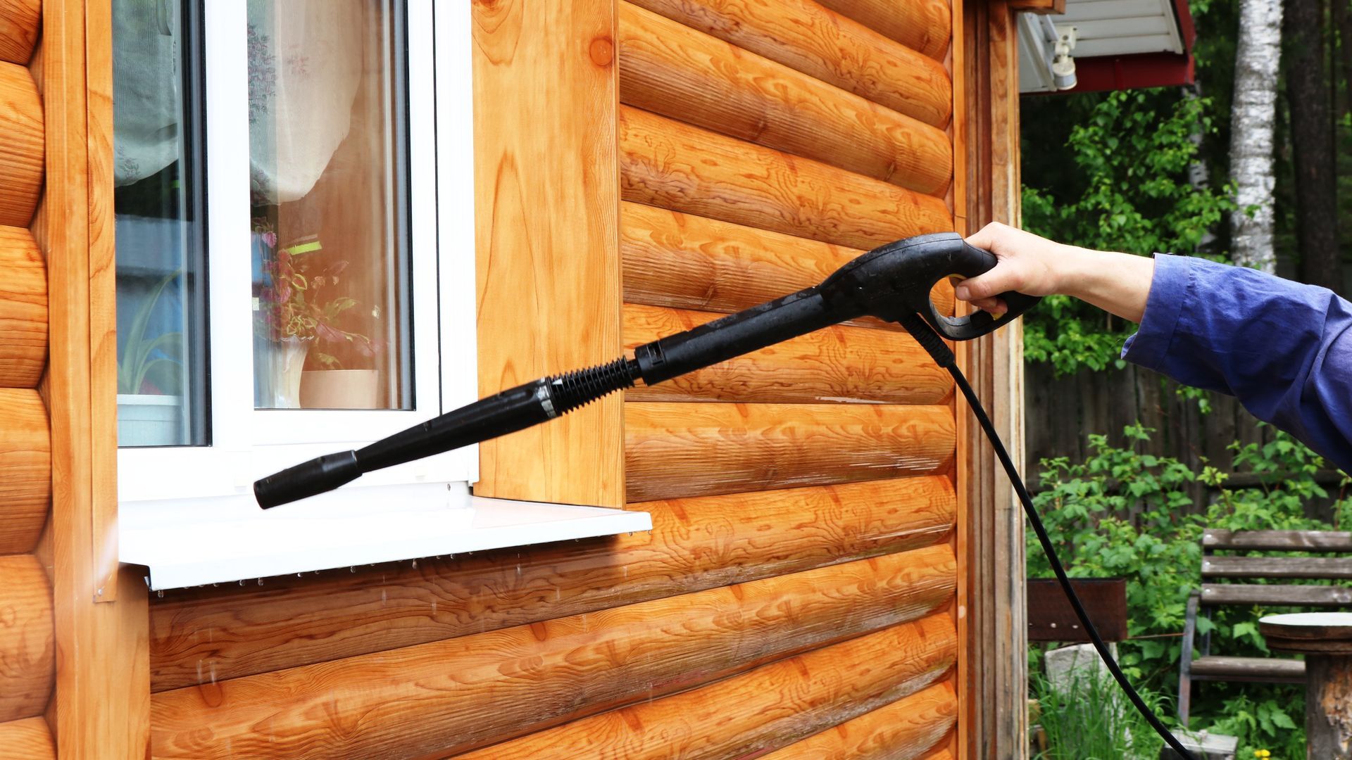 A person is cleaning a log cabin with a high pressure washer.