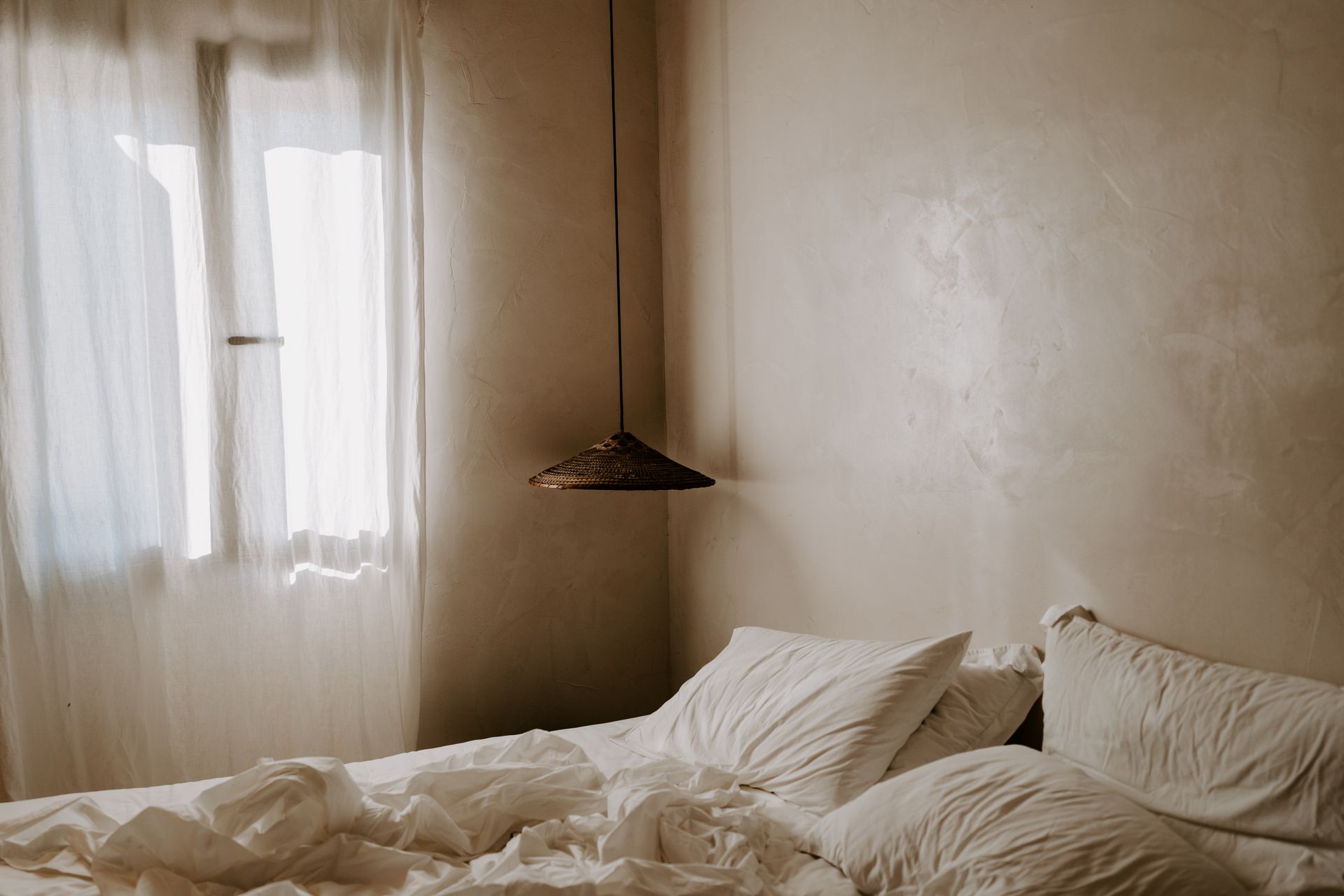 A bed with white sheets and pillows in a bedroom next to a window.