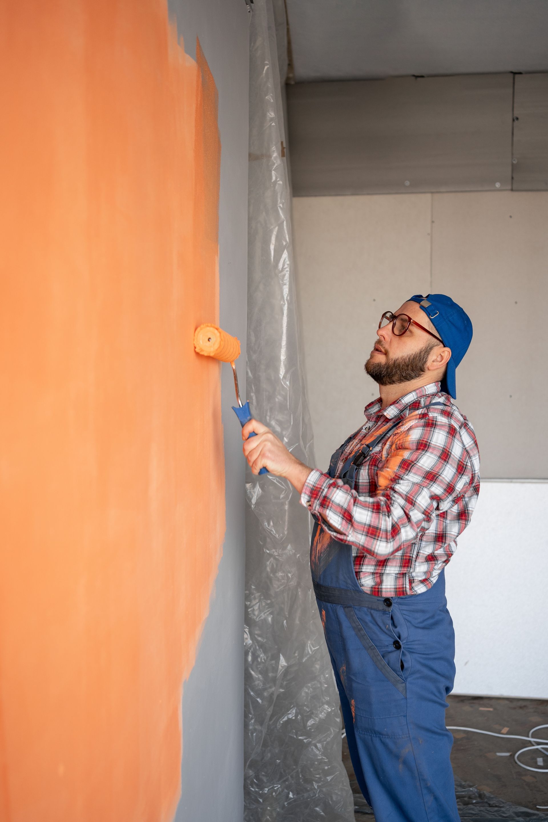 A man is painting a wall with an orange paint roller.