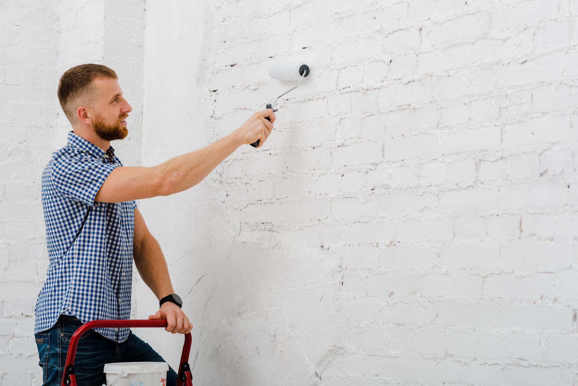 A man is painting a white brick wall with a paint roller.