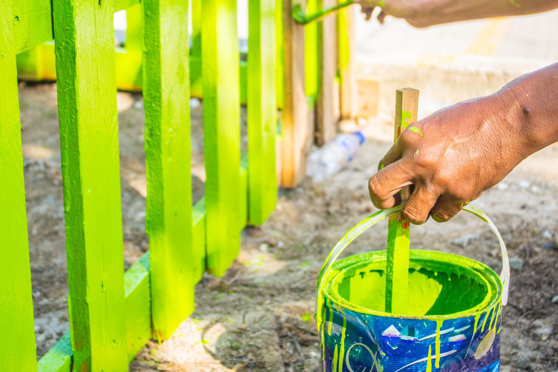 A person is painting a fence with green paint.