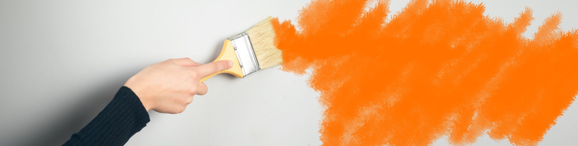 A person is painting a wall with orange paint.