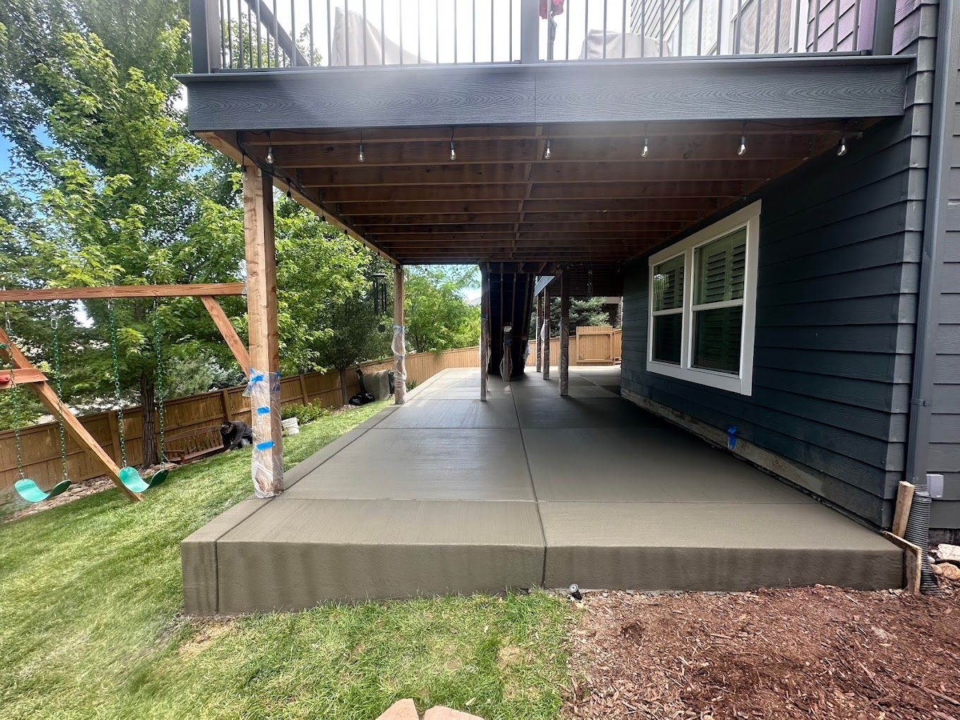 A concrete patio under a deck in the backyard of a house.