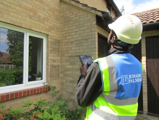 Worker in high-vis vest inspecting a house exterior with a tablet beside a window