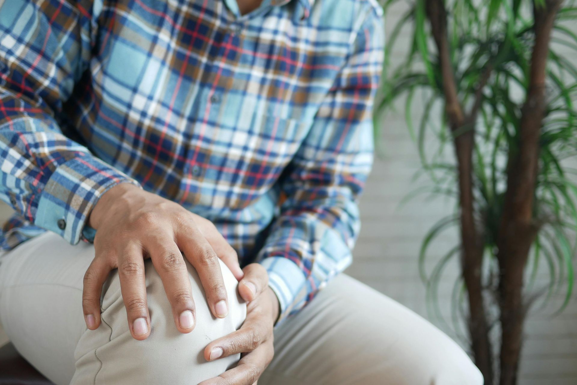 A man is sitting on a couch holding his knee in pain.