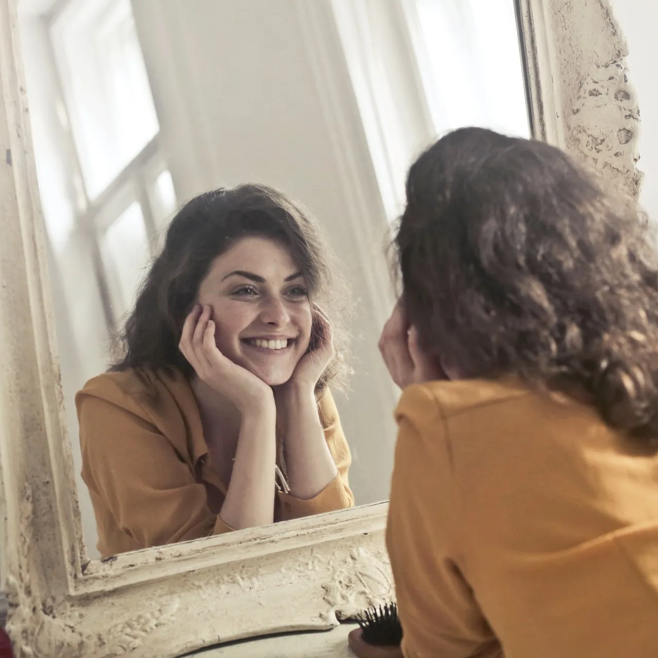 A woman is smiling while looking at herself in a mirror