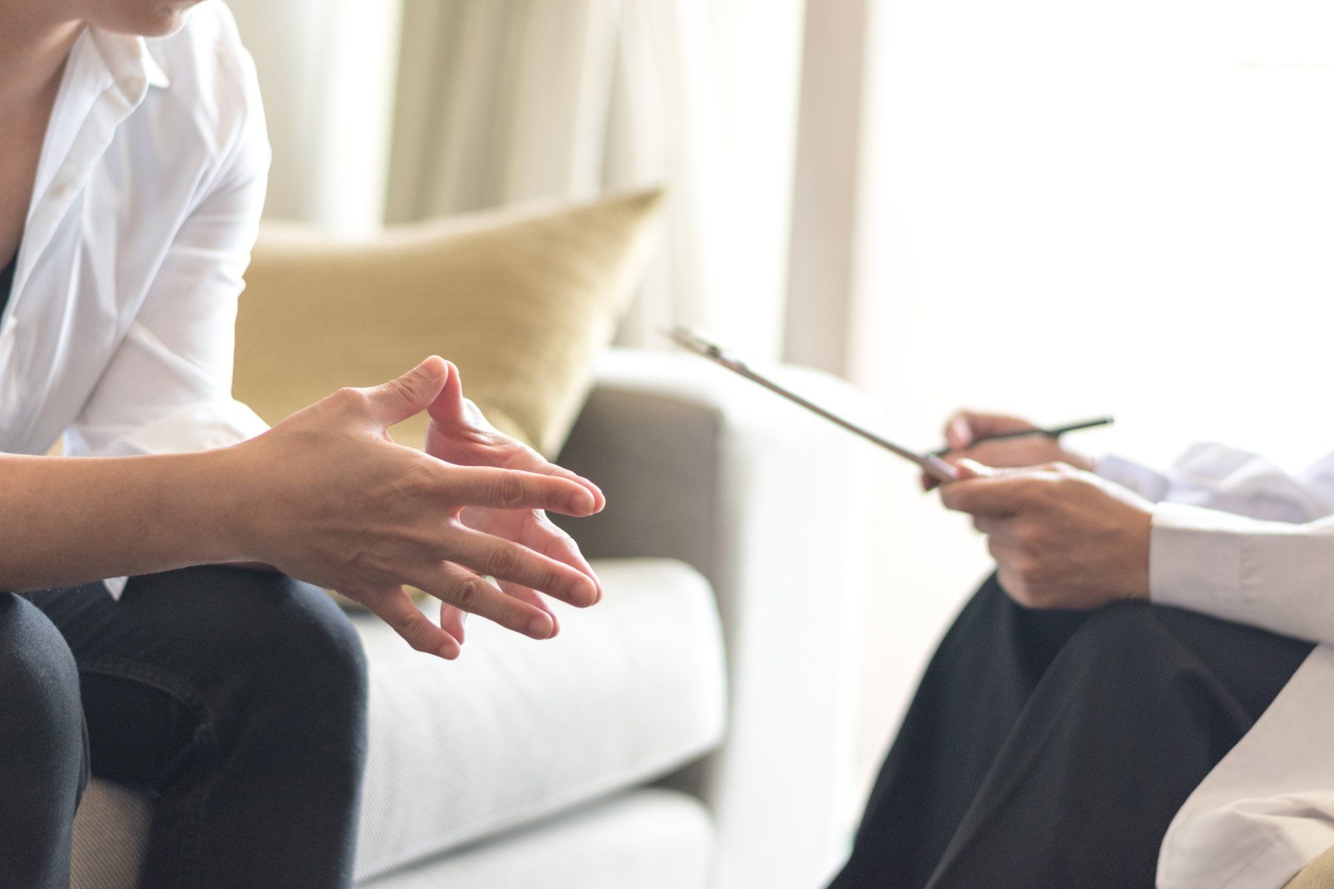 a woman is sitting on a couch talking to a doctor who is holding a clipboard . therapy for adults representation.