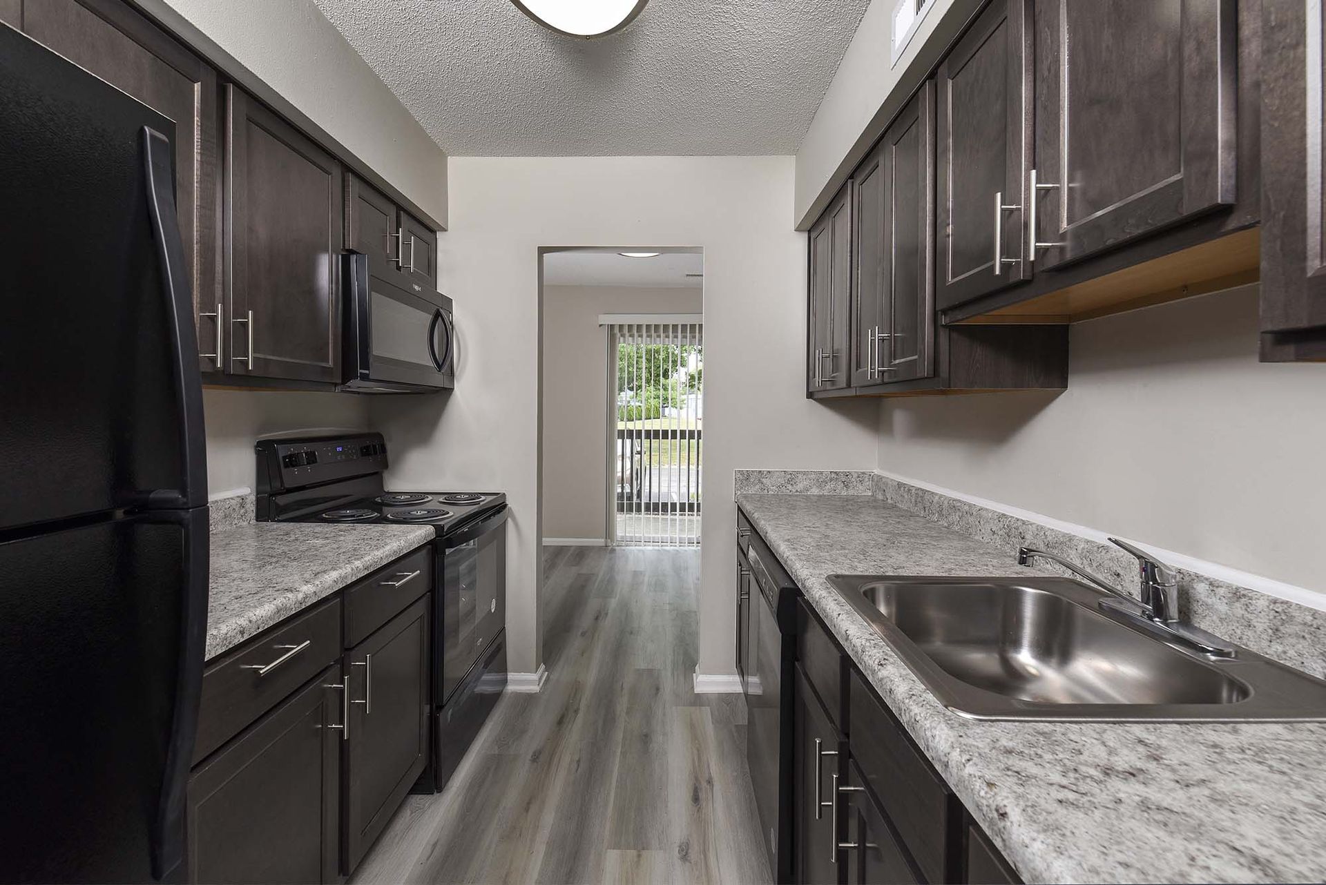 Galley kitchen in an apartment with dark wood cabinets, grey countertops, and stainless steel appliances.