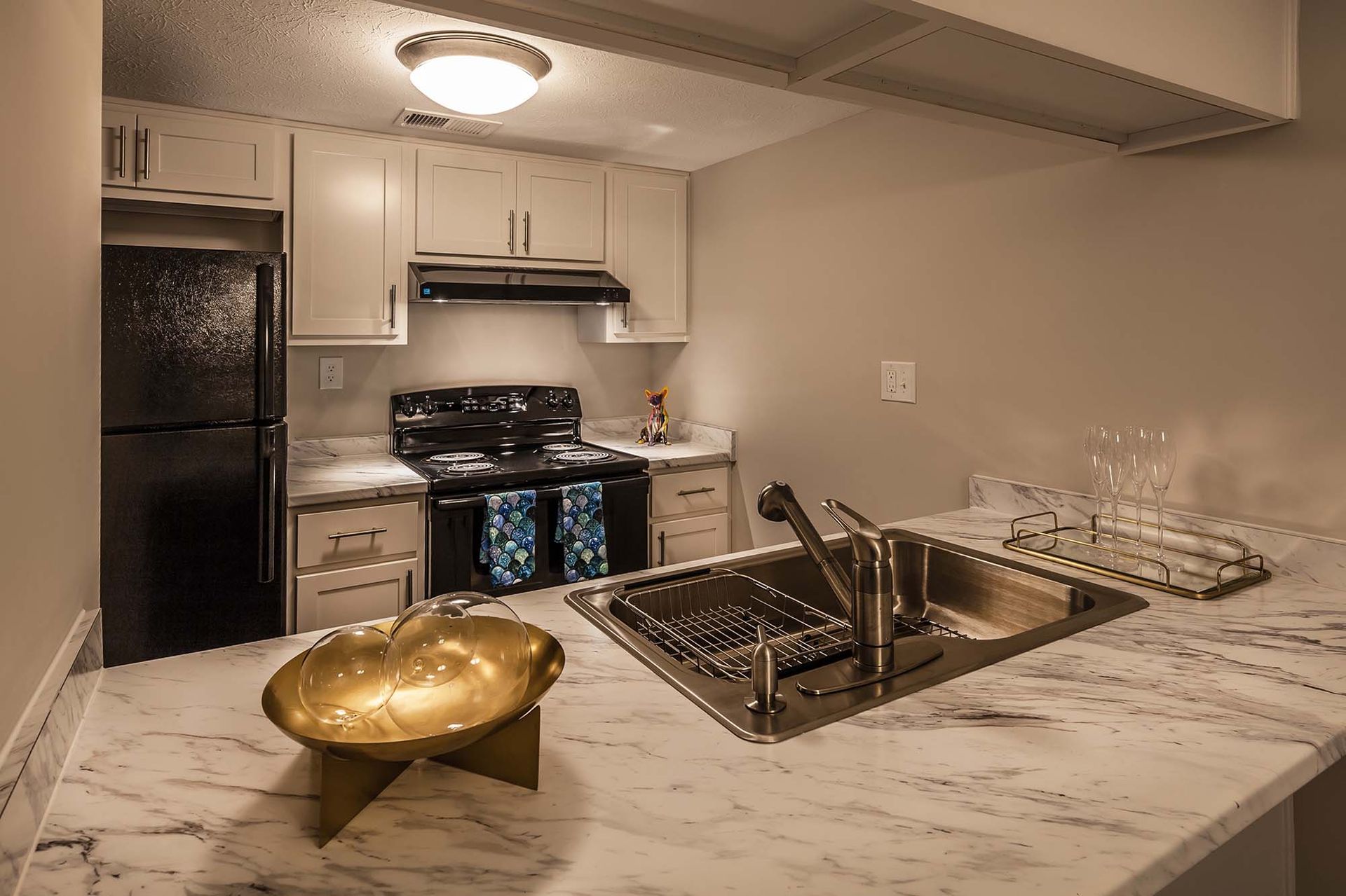 Modern apartment kitchen with marble countertops, white cabinets, a black range, and a double sink.