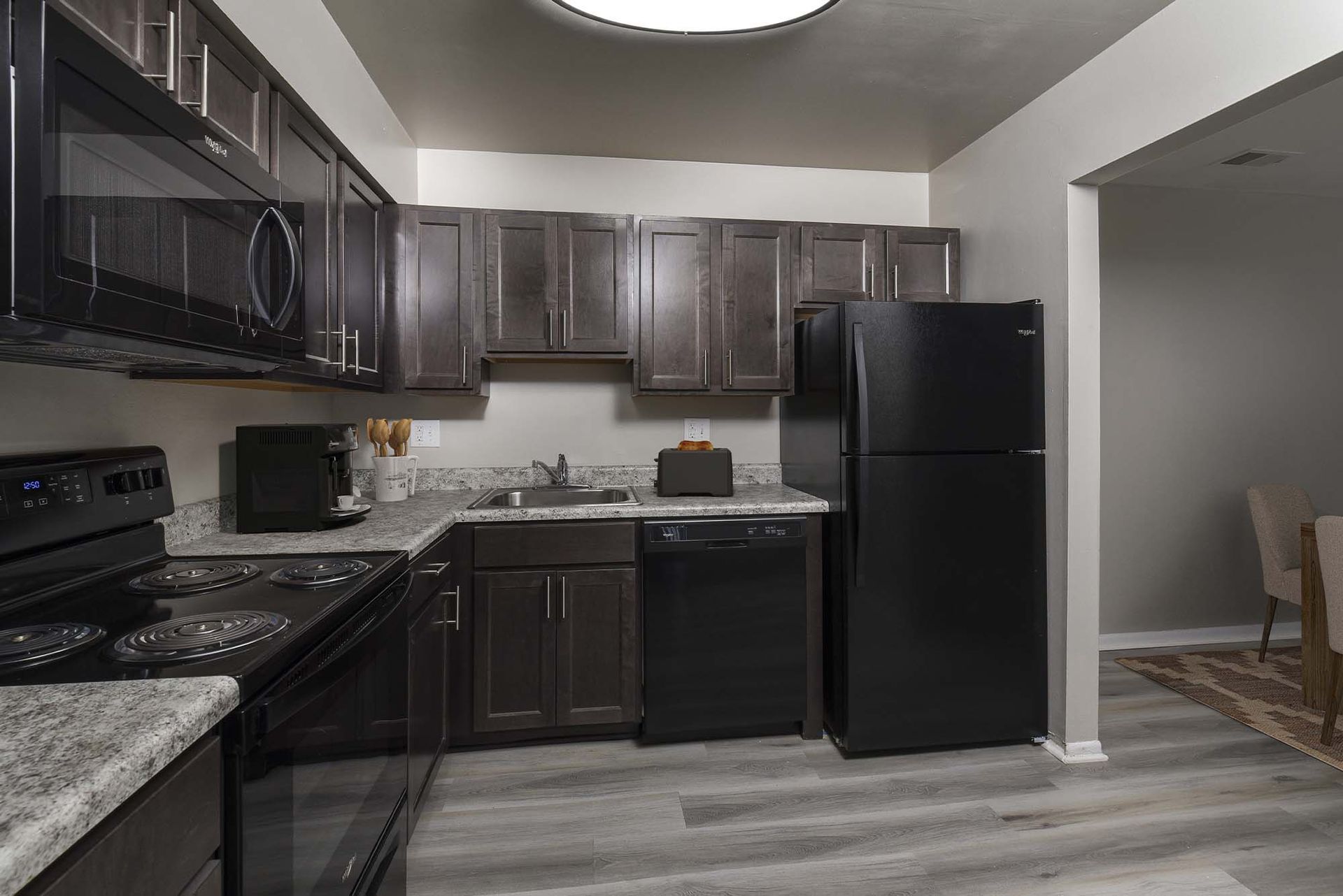 Apartment kitchen with dark wood cabinets, black appliances, and granite countertops.