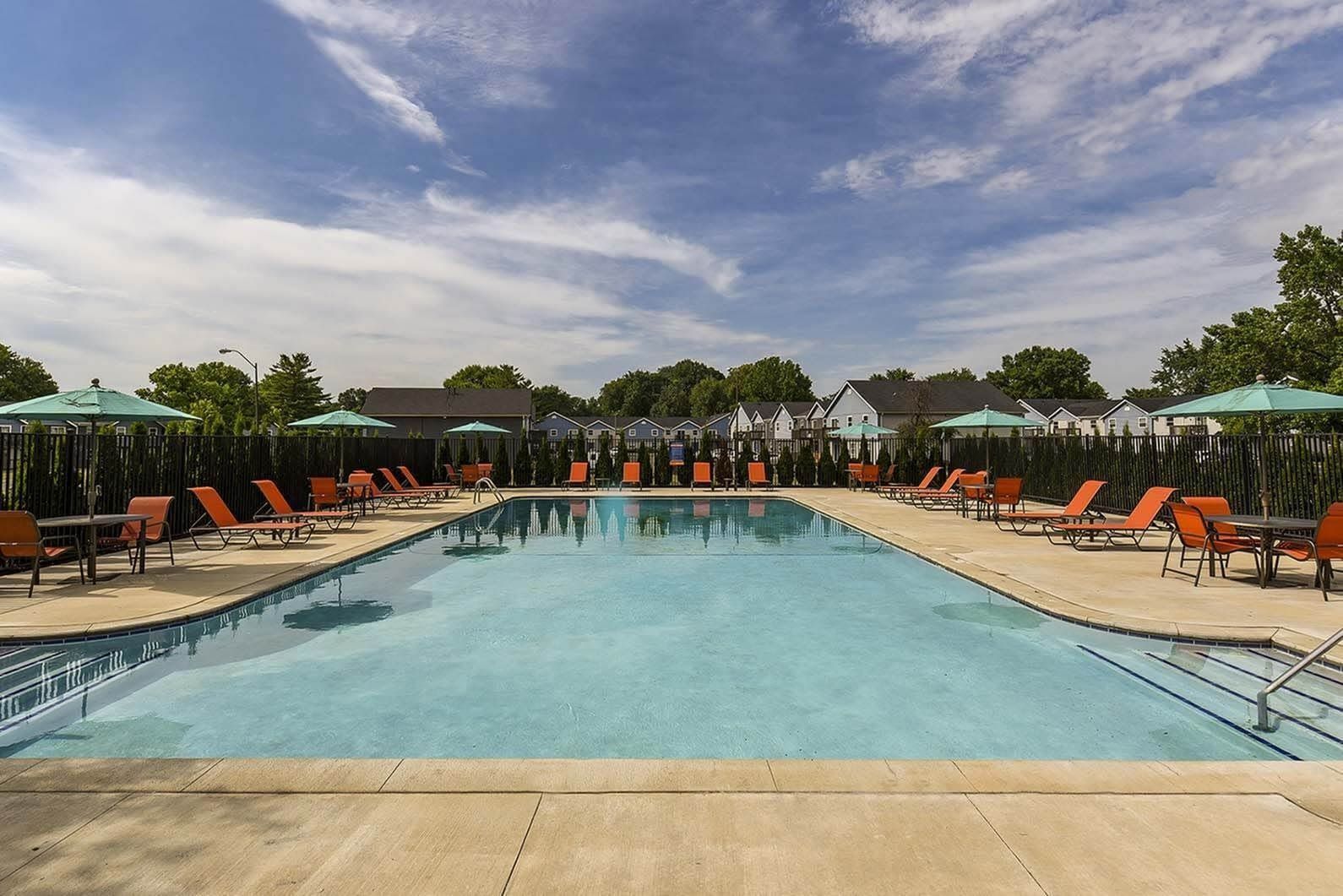 Outdoor community pool with orange lounge chairs and umbrellas.