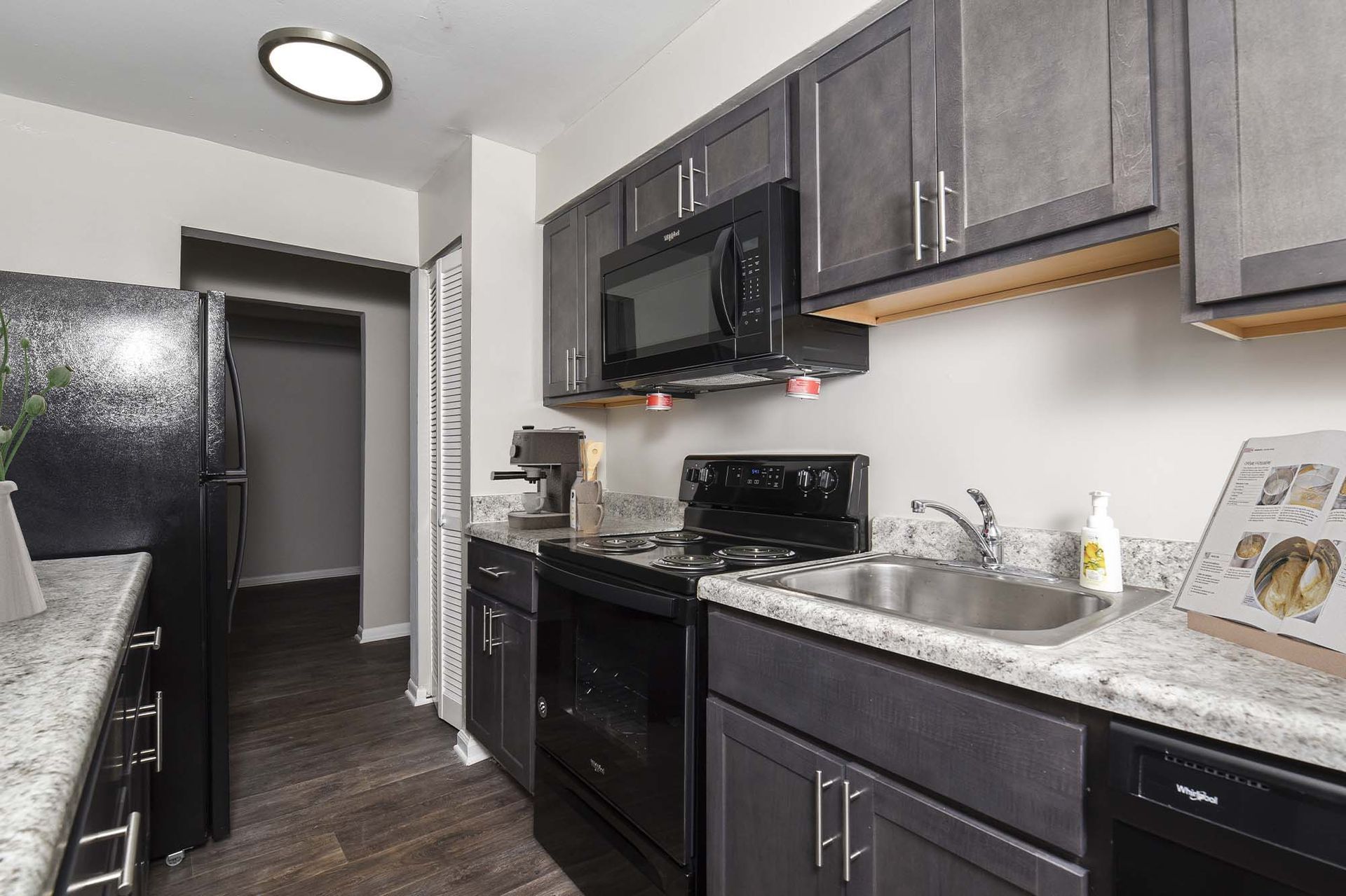 Compact modern apartment kitchen with dark cabinets, black appliances, and a stainless sink.