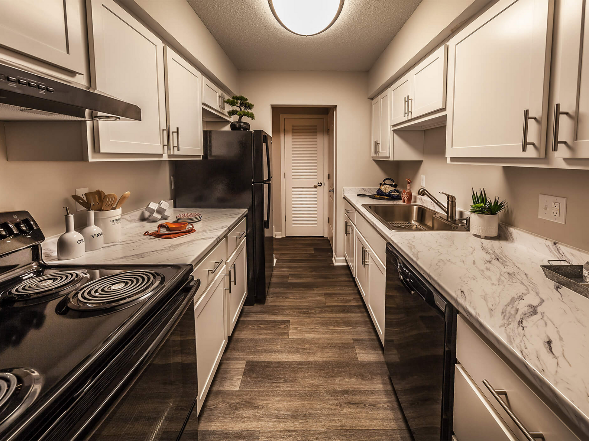 Narrow galley kitchen with white cabinets, marble countertops, and stainless steel appliances.