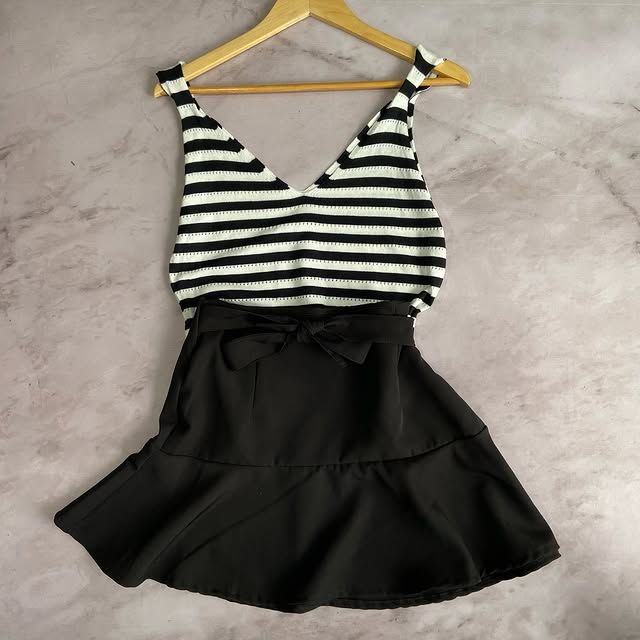 Top de rayas blancas y negras y falda negra con lazo, colgado en una percha de madera.