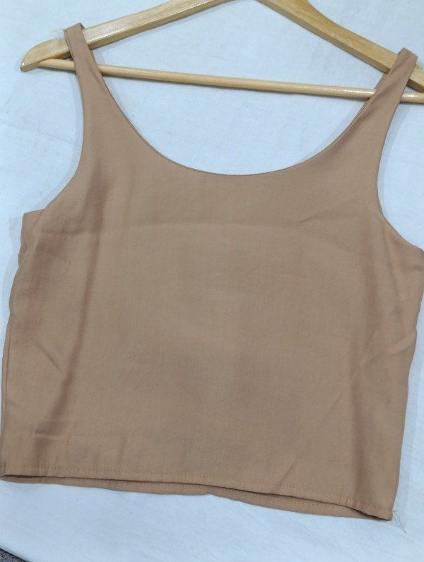 Camiseta sin mangas de color bronce y cuello redondo colgada en una percha de madera.